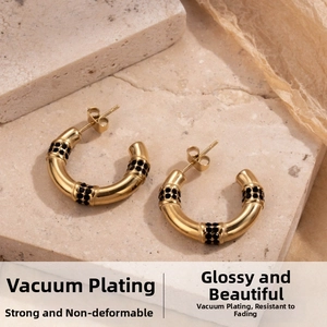 Detail of C-shaped gold hoop earrings with black micro-inlaid stones on stone surface