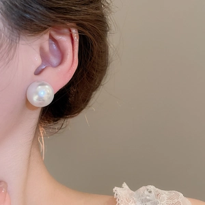 Macro view of elegant large pearl stud earrings worn by model with warm lighting