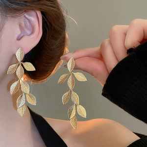 Close-up of elegant gold leaf tassel earrings with textured metal finish on model
