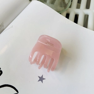 Gros plan sur une pince à cheveux rose en acétate avec texte posée sur un magazine