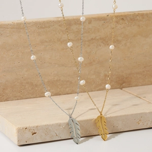 Elegant gold and silver feather leaf pendant necklace with pearl on stone background
