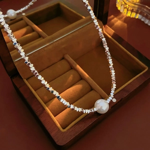 Detailed view of silver bead necklace with a white pearl pendant on brown velvet lining