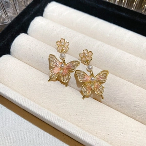 Détail de boucles d'oreilles papillon avec dégradé de rose et accents de perles