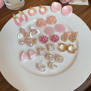 Detailed overhead view of elegant pink flower earrings and faux pearl studs on a tray