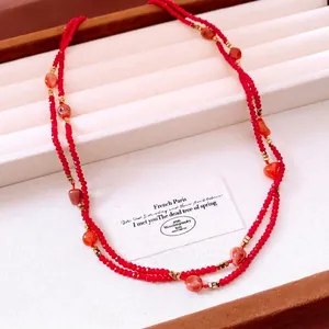 Elegant red glass beaded necklace with orange stone accents on a white jewelry tray