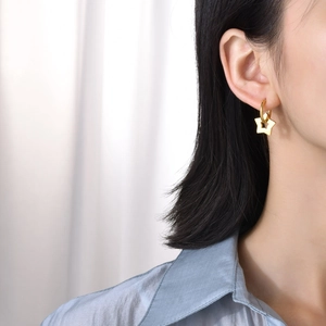 Close-up of a woman wearing gold star charm hoop earrings in a minimalist style