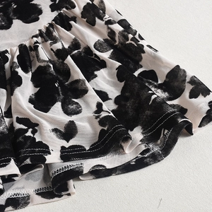 Détail du tissu en maille blanc cassé avec flocage floral noir et bords à volants