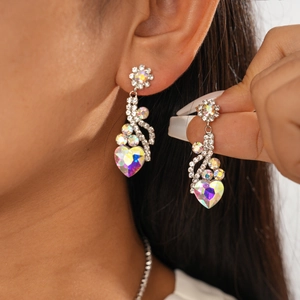 Détail de boucles d'oreilles fleur et cœur en cristal argenté portées par un modèle