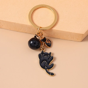 Detail shot of black cat keychain with golden ring and bell on a textured surface