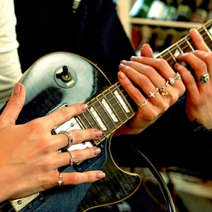 Detail shot of hand wearing silver zircon rings while playing guitar in warm lighting