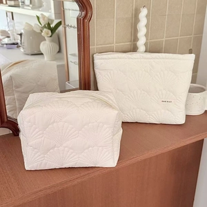 Set of two cream quilted makeup bags with shell pattern on a warm wooden table