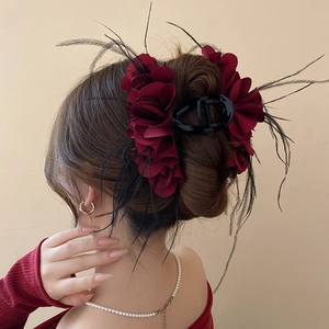 Detail of burgundy floral hair claw with delicate feathers and ruffled fabric petals