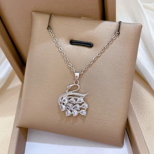 Close-up of a silver swan pendant necklace with clear crystals on a beige display pad