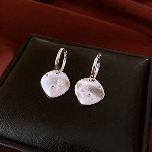 Close-up of silver rhombus earrings with brushed texture, pearl accents and zircon stones