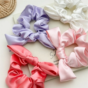 Detail view of four satin bow scrunchies in purple, white, pink and coral rose colors