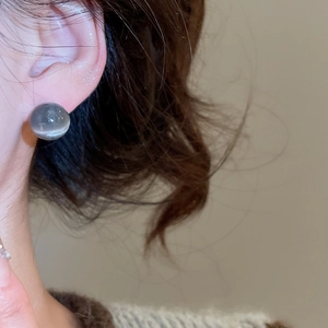 Gros plan d'une boucle d'oreille ronde en résine grise portée pour un style décontracté