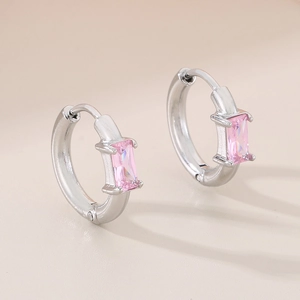 Gros plan de boucles d'oreilles créoles argentées avec un zircon rose carré