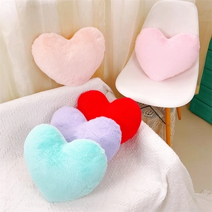 Coussins décoratifs en peluche en forme de cœur en diverses couleurs sur un lit