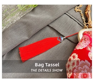 Close-up of red tassel accessory with cloisonné cloud detail on embroidered shell bag