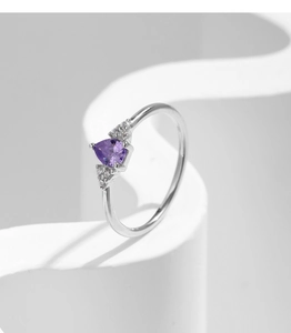 Detail view of heart-shaped purple amethyst ring with diamond accents on white pedestal