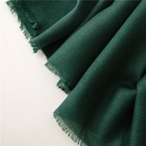 Detalle de bufanda de tela verde oscuro con flecos finos y textura tejida suave