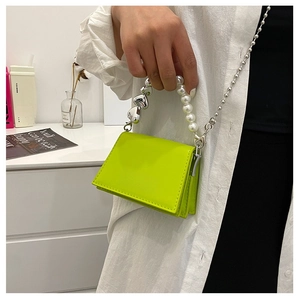 Detail of neon green mini bag with pearl heart handle and fine silver chain strap