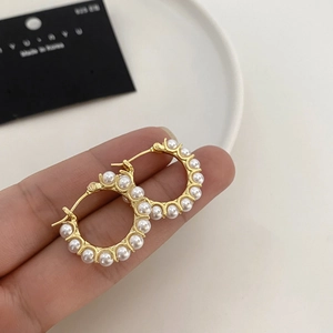 Macro shot of gold-plated hoop earrings with pearls held by hand to show size