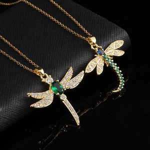 Detail of two gold dragonfly necklaces with emerald and blue zircon on leather box