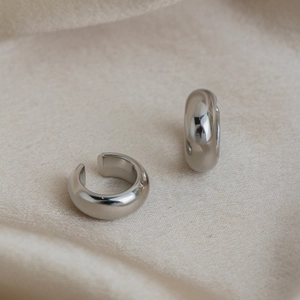 Dettaglio macro di ear cuff minimalisti in argento su seta beige con luce soffusa