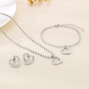 Détail d'un ensemble collier bracelet et boucles d'oreilles cœur argenté sur table beige
