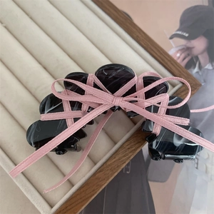 Detail of black marble acetate hair claw with pink ribbon bow on a beige velvet tray