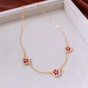 Detailed close-up of an 18K gold-plated flower pendant necklace with red cubic zirconia
