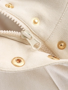 Détail macro du tissu en daim beige avec bouton pression doré et fermeture éclair crème
