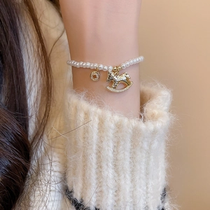 Detail shot of a beaded pearl bracelet with a golden rocking horse and rhinestone pendant