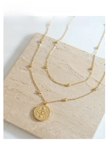 Detail view of a gold double-layer necklace with an evil eye coin pendant on stone