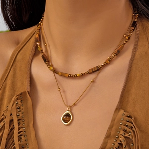 Detail view of double-layer Tiger Eye stone necklace with golden pendant on brown sweater
