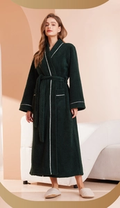 Close-up of women's dark green long warm robe with white piping and plush velvet texture