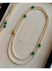 Detail of double-layer faux pearl necklace with green beads in a beige jewelry box