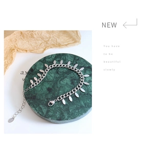 Close-up of silver titanium steel bracelet with oval charms on green marble stand