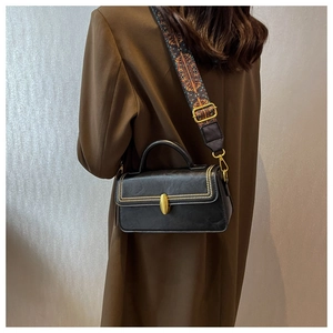 Detail of a vintage black leather crossbody bag featuring gold studs and a woven strap