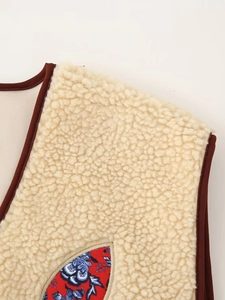 Close-up of beige faux shearling vest featuring a floral patch pocket and brown piping