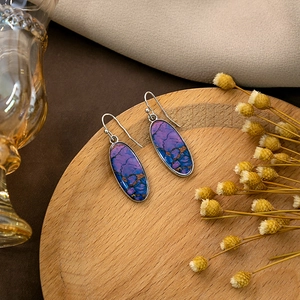 Detail of oval drop earrings with purple blue stone texture on a wooden tray