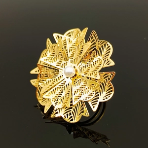 Macro detail of gold layered hollow flower ring with a white pearl on black surface