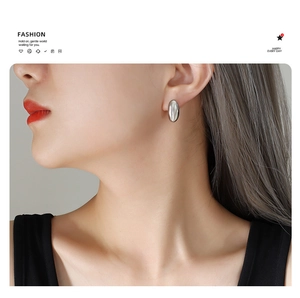 Macro detail of polished silver oval stud earring on model showing minimalist fashion style