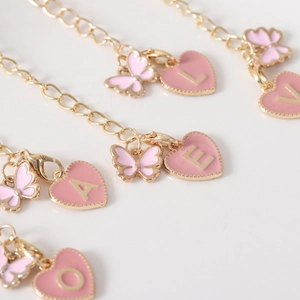 Macro shot of gold chains with pink enamel heart letters and butterfly charms for tumblers