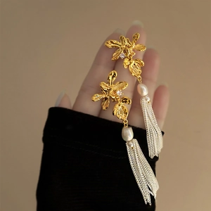 Détail de boucles d'oreilles fleur dorée avec perle blanche et pompons argentés