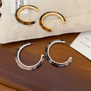 Detail of C-shaped resin earrings in tortoise shell and marble textures with metal frames
