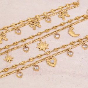 Detailansicht goldener Armbänder mit Sonne, Mond, Schleife und Zirkon-Anhängern auf Sandstein