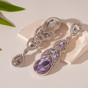 Detailed view of teardrop earrings with purple and white crystals on stone surface