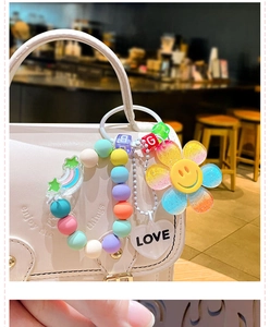 Close-up of rainbow smiling flower bead charm on a stylish white handbag strap